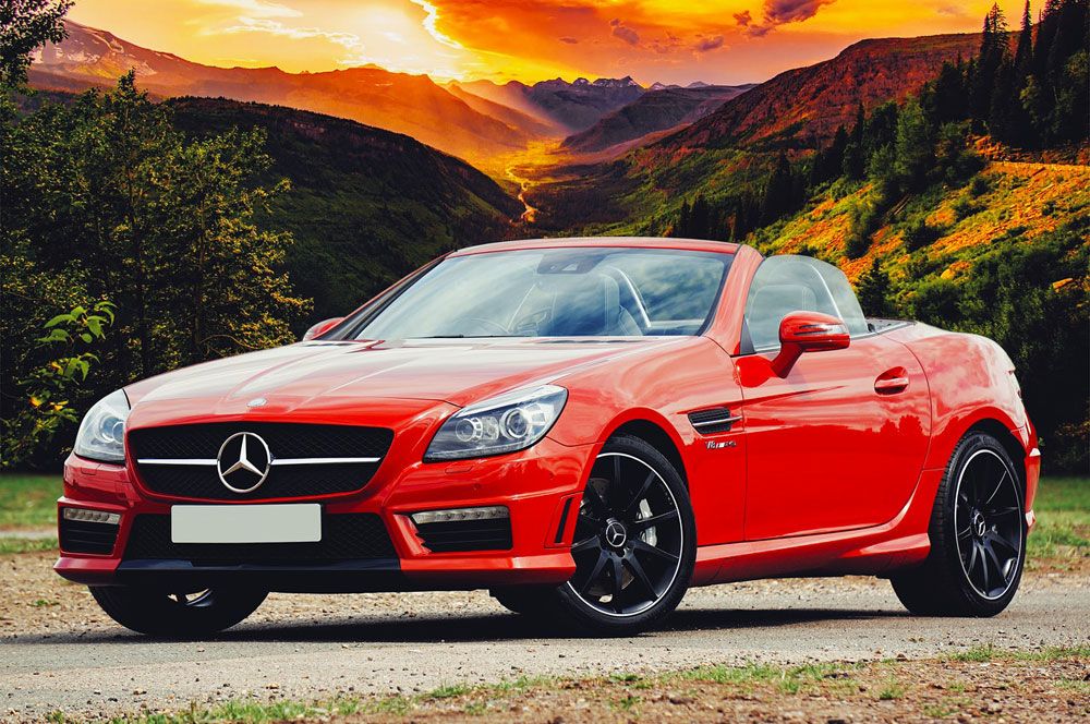 Red Mercedes-Benz SLK roadster in front of green hills at sunset